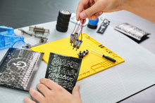 Load image into Gallery viewer, Person assembling electronic components on a workbench with tools and materials.