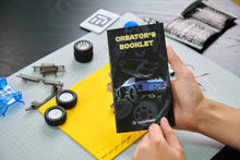 Load image into Gallery viewer, Person holding a 'Creator's Booklet' with model building components on a table