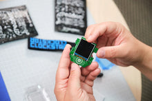 Load image into Gallery viewer, Person holding a small electronic device with a screen, likely a microcontroller or similar component, on a blurred background.