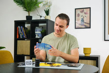 Load image into Gallery viewer, Man holding a blue object in a room with furniture and decor
