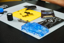 Load image into Gallery viewer, Blue plastic model car on a white mat with tools and parts on a dark surface
