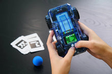 Load image into Gallery viewer, Hand holding a transparent electronic device with a screen, next to cards and a blue ball on a dark surface.
