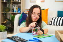 Load image into Gallery viewer, Woman working on a craft project at a table with various materials and tools.

