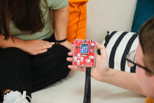Load image into Gallery viewer, Person holding a small red electronic device with a screen, sitting on a couch.
