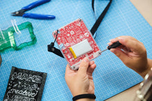 Load image into Gallery viewer, Person assembling a small electronic device on a blue cutting mat with tools and materials around.
