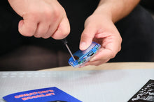 Load image into Gallery viewer, Person using a screwdriver on a small electronic component on a table with a mat.
