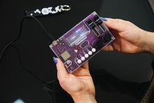 Load image into Gallery viewer, Purple electronic circuit board held by a person against a dark background

