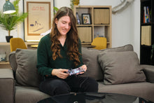 Load image into Gallery viewer, Woman playing a video game on a console in a living room.
