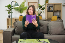 Load image into Gallery viewer, Woman holding a purple book in a living room setting
