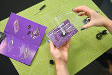 Load image into Gallery viewer, Person holding a clear plastic component over a purple printed circuit board on a green cutting mat.
