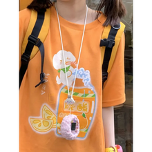 Load image into Gallery viewer, Person wearing an orange shirt with a cartoon design, holding a lanyard with a small bag.
